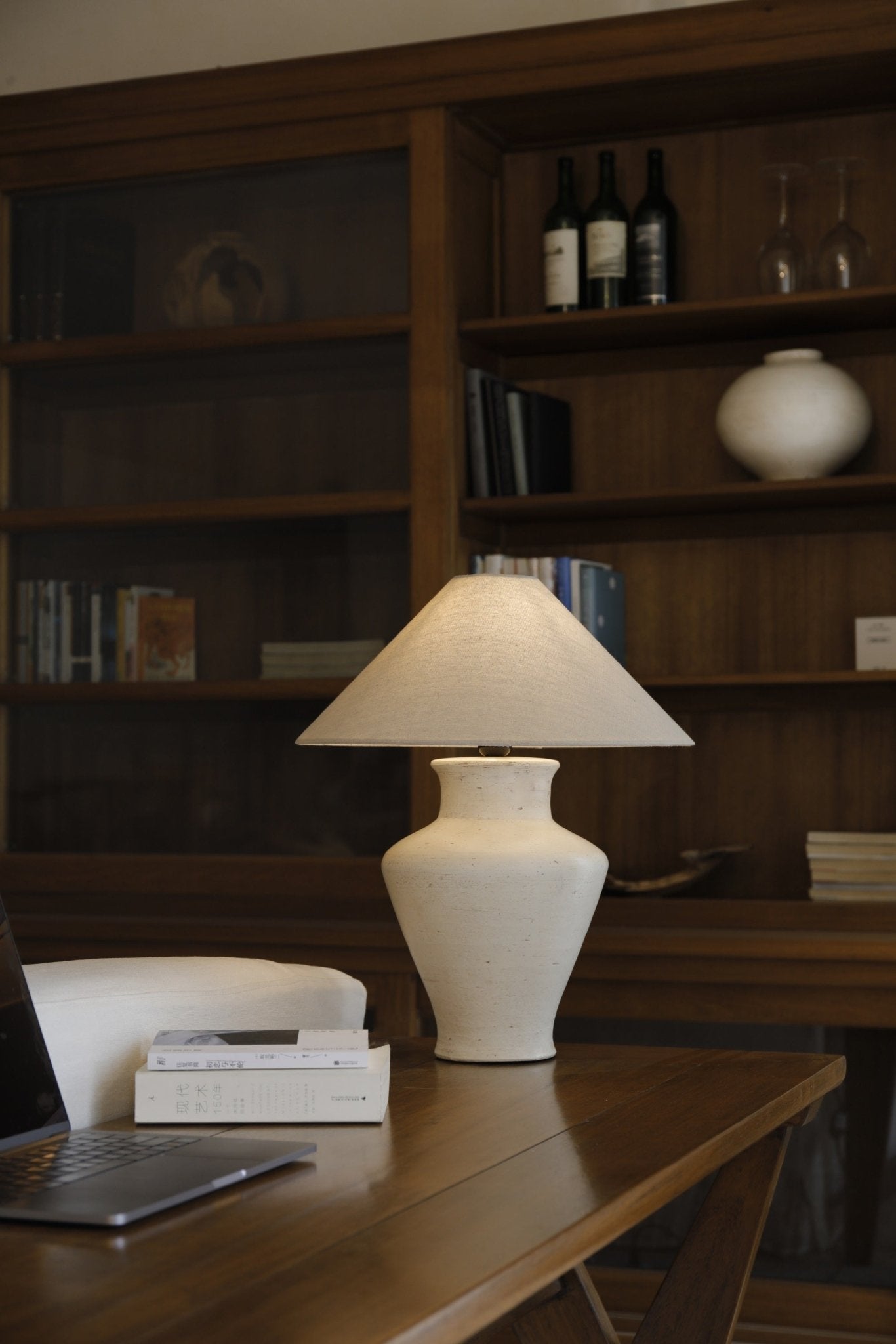 Short neck lamp with clay base and linen shade on wooden table, modern design