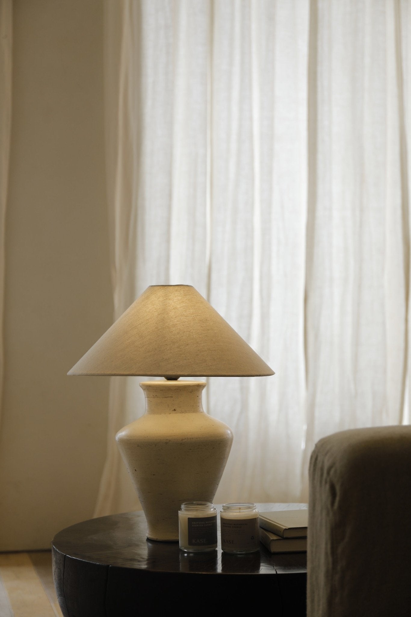 Cream clay base short neck lamp with linen shade on a wooden table, interior design.