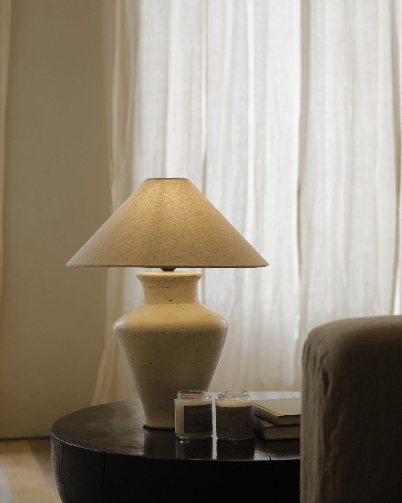 Cream clay base short neck lamp with linen shade on a wooden table, interior design.