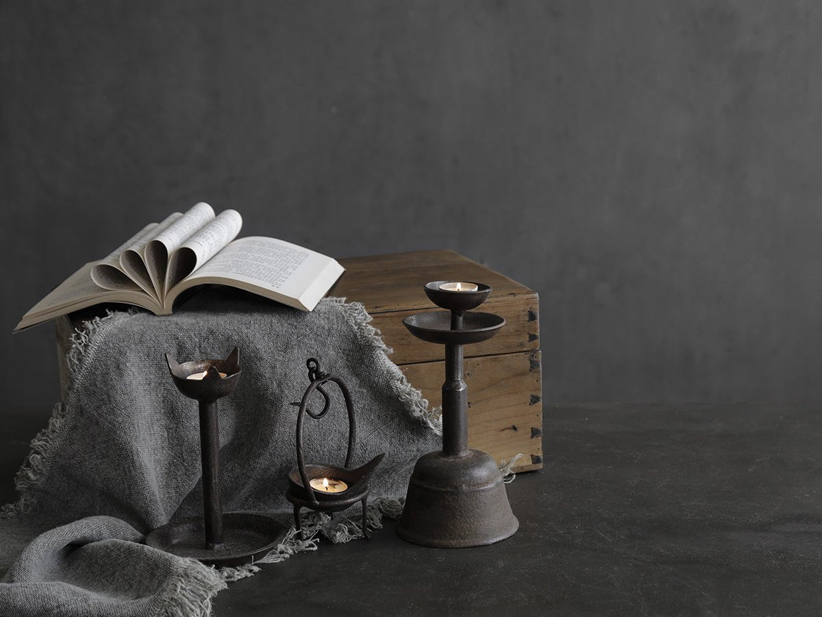 Rustic iron candle holder set with lit candles, creating a warm ambiance for home decor, styled with book and fabric.