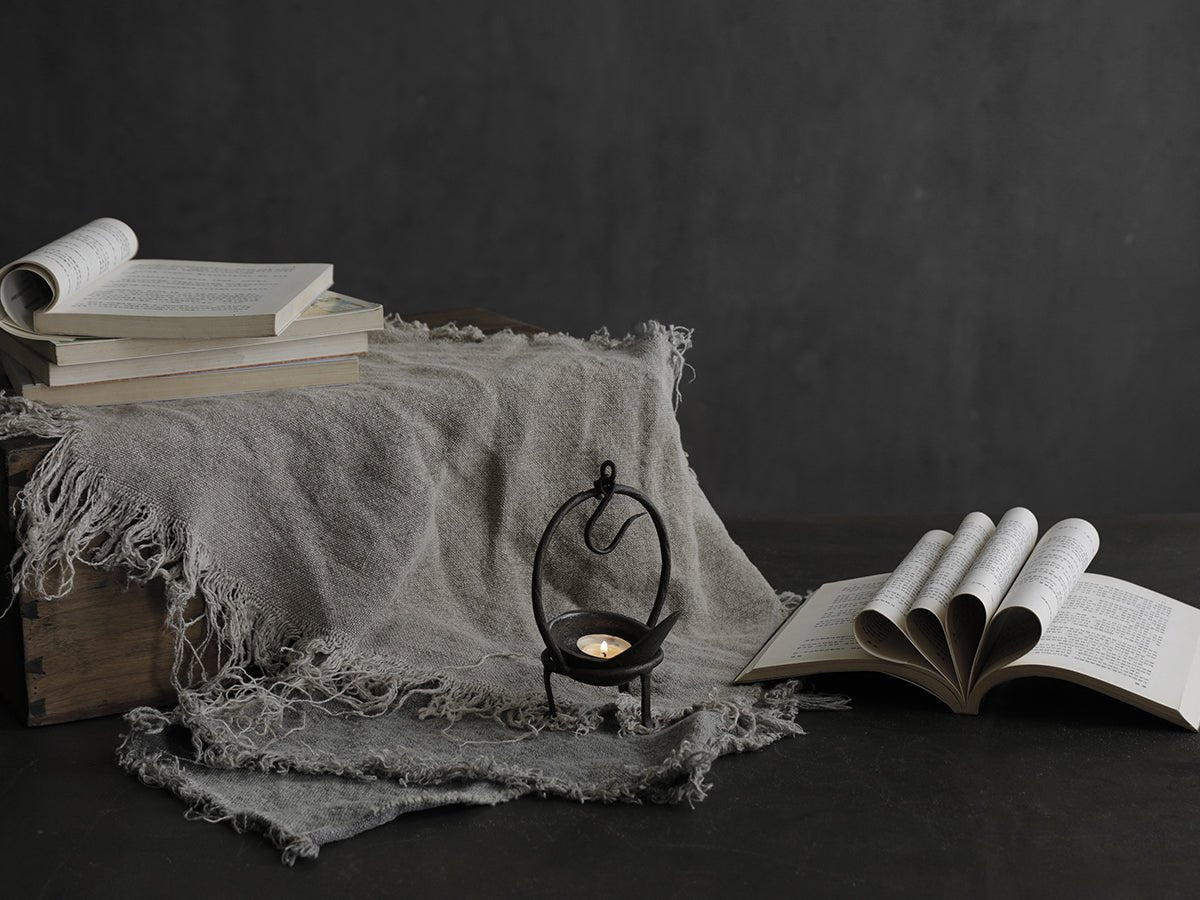 Rustic iron candle holder with lit candle, books, and linen cloth, creating a cozy home decor ambiance