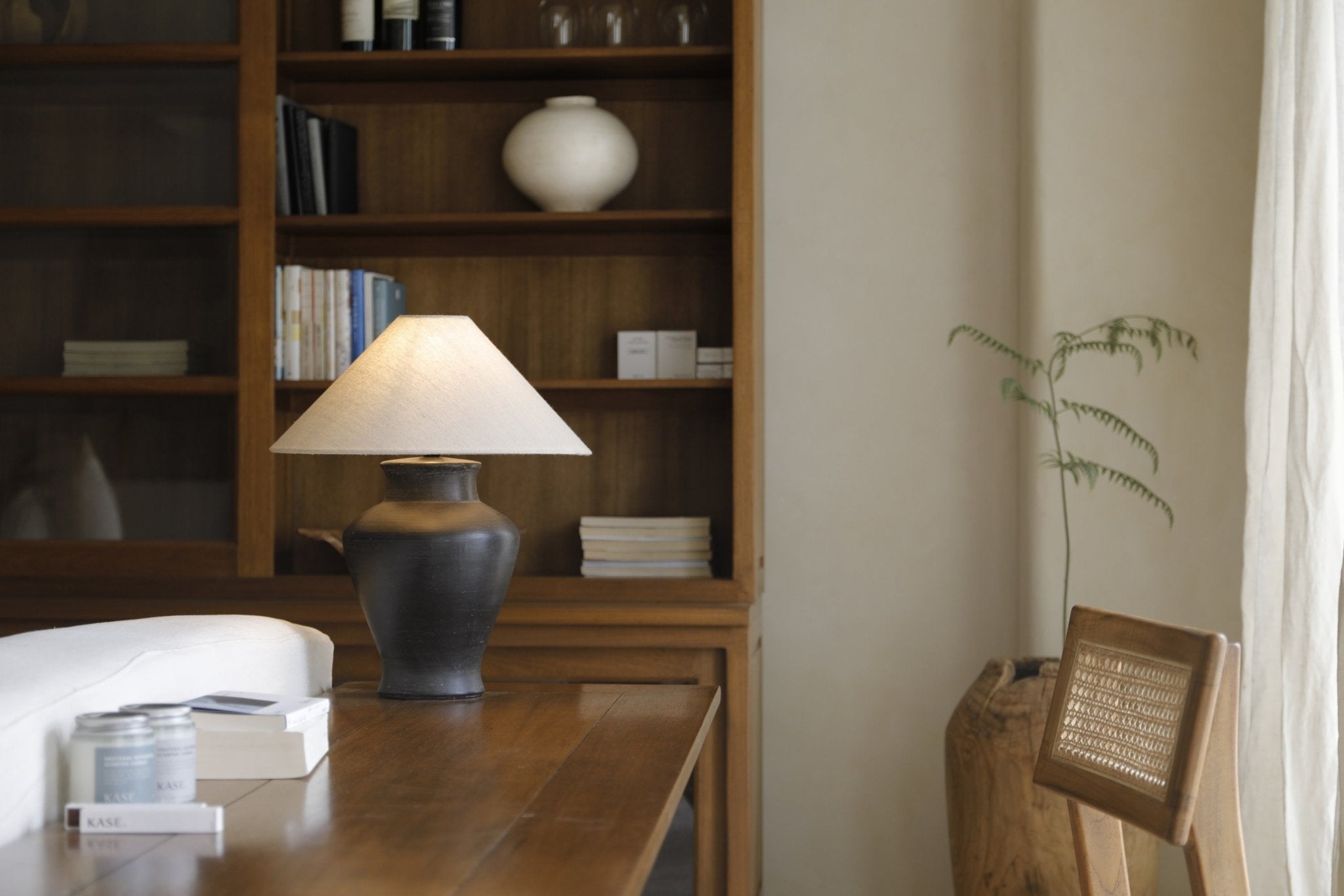 Short neck lamp with clay base and linen shade on wooden table, interior design.