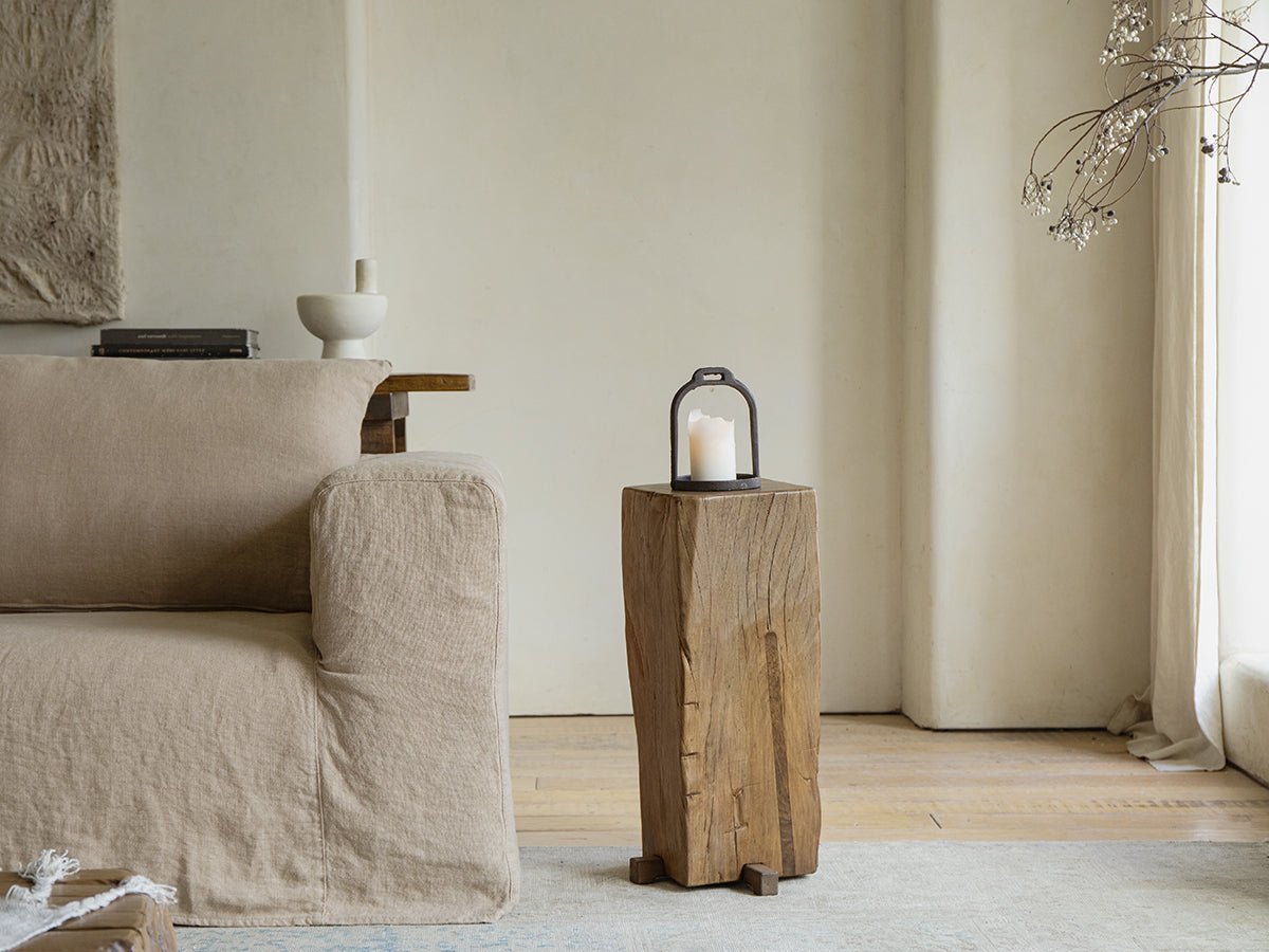 Rustic pedestal side table with candle, organic interior design, aged wood texture, timeless simplicity