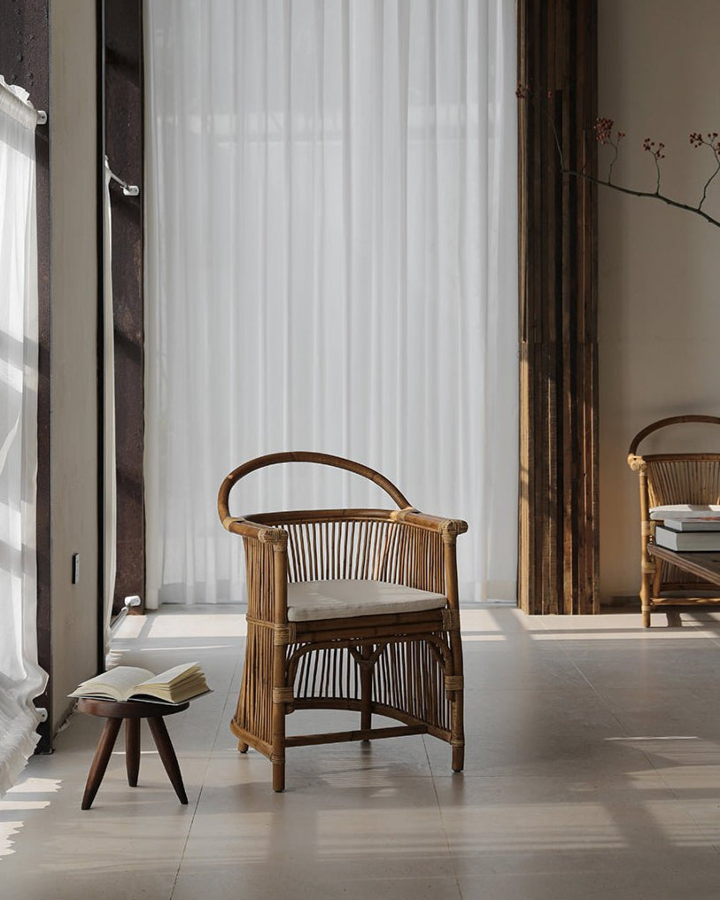 Cape Chair in natural rattan with hanging backrest, linen cushion, and a book on a wooden stool, stylish interior