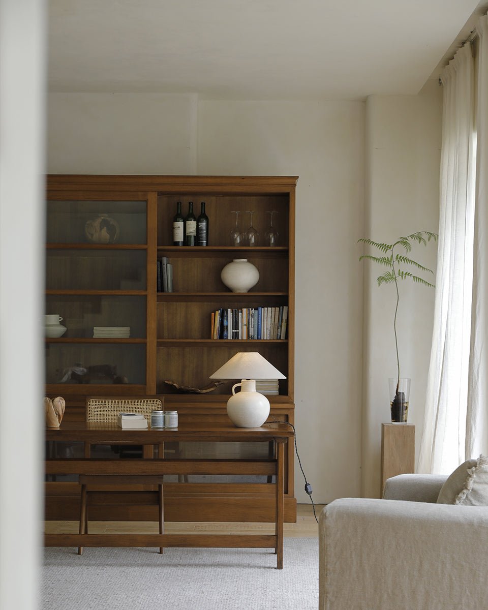 African teak glass bookcase, displaying books, wine, and a lamp, an elegant storage solution for living room.