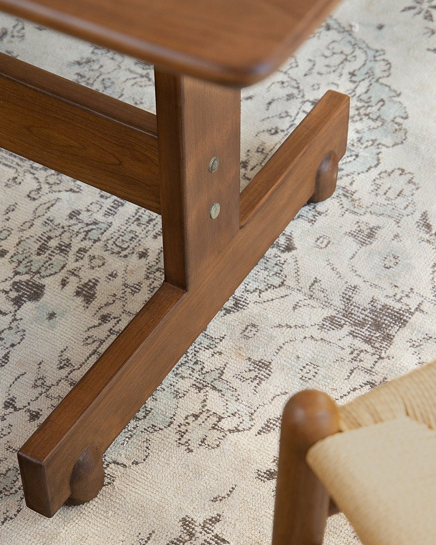 Hoof Dining Table's solid wood I-shaped base in warm brown finish, showcasing the table's stability and design.