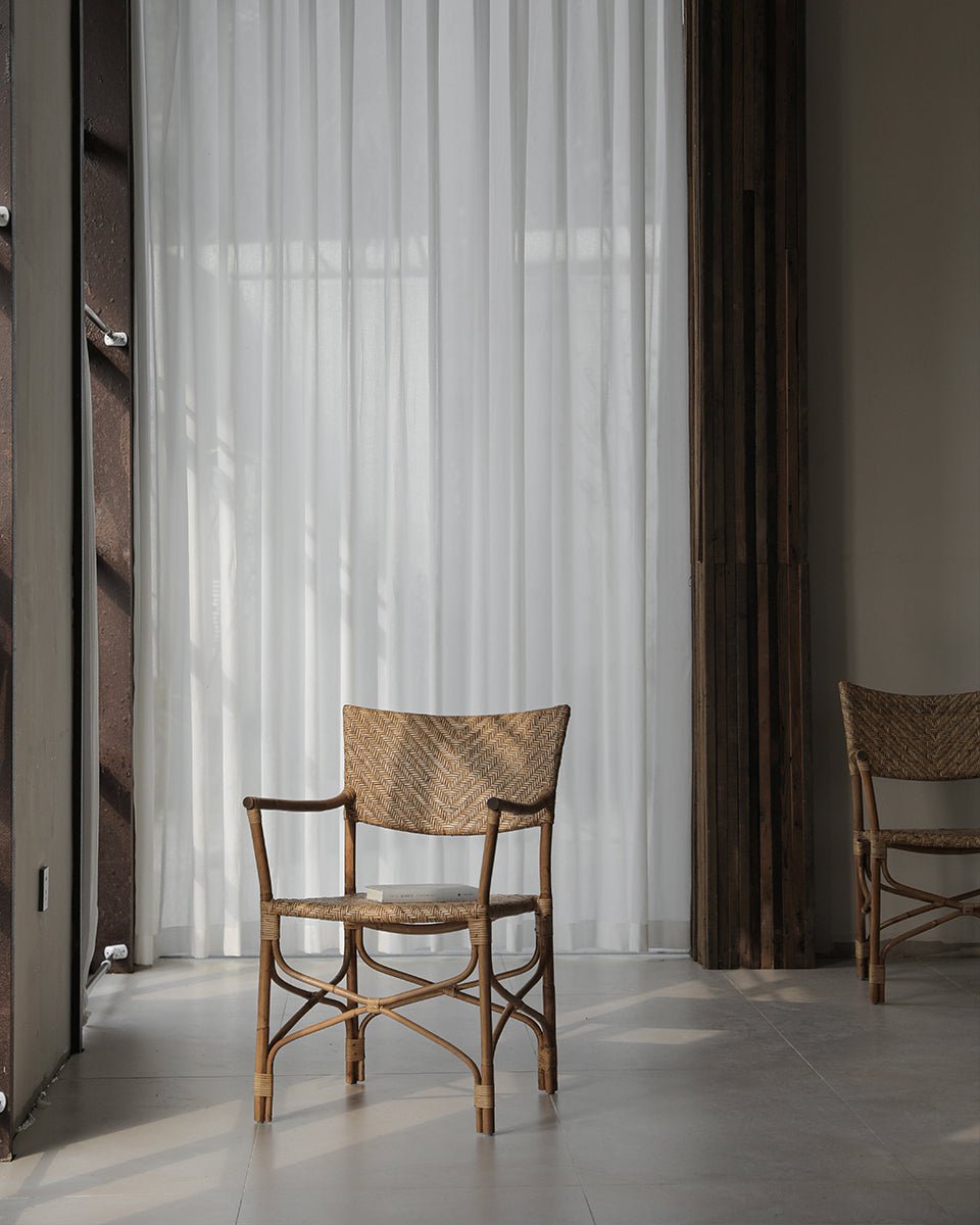 Dingee Chair with woven back, natural wood frame, and armrests, showcased against a backdrop of sheer curtains.