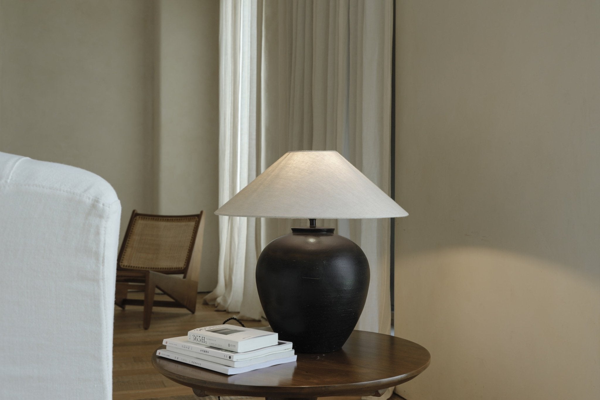 Modern black clay Egg Lamp on wooden side table next to white sofa, interior decor, and books