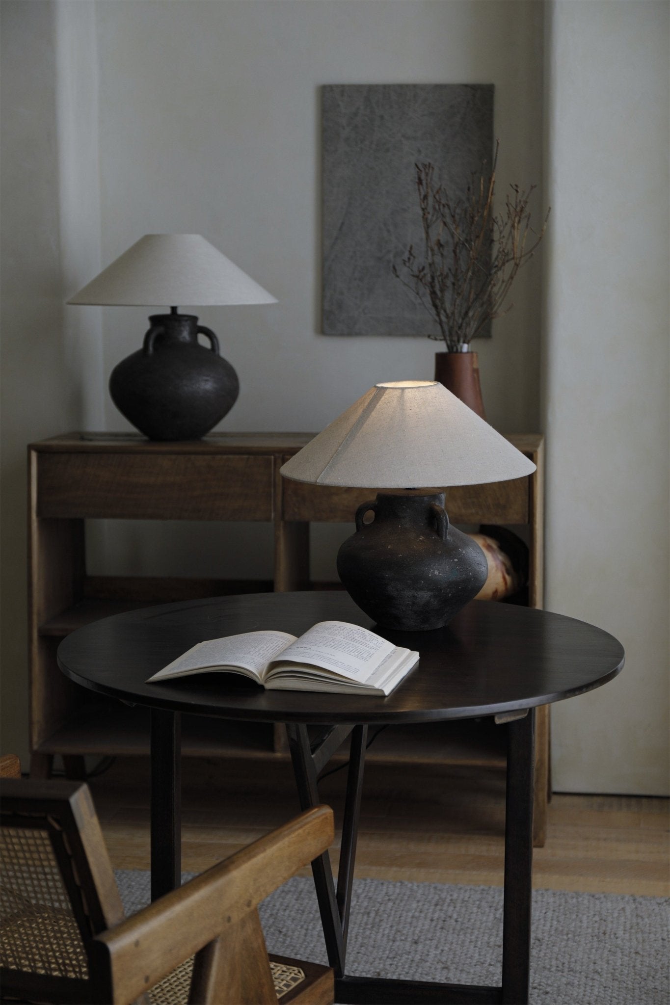 Ear lamp with dark clay base, off-white shade, and book on a round table.