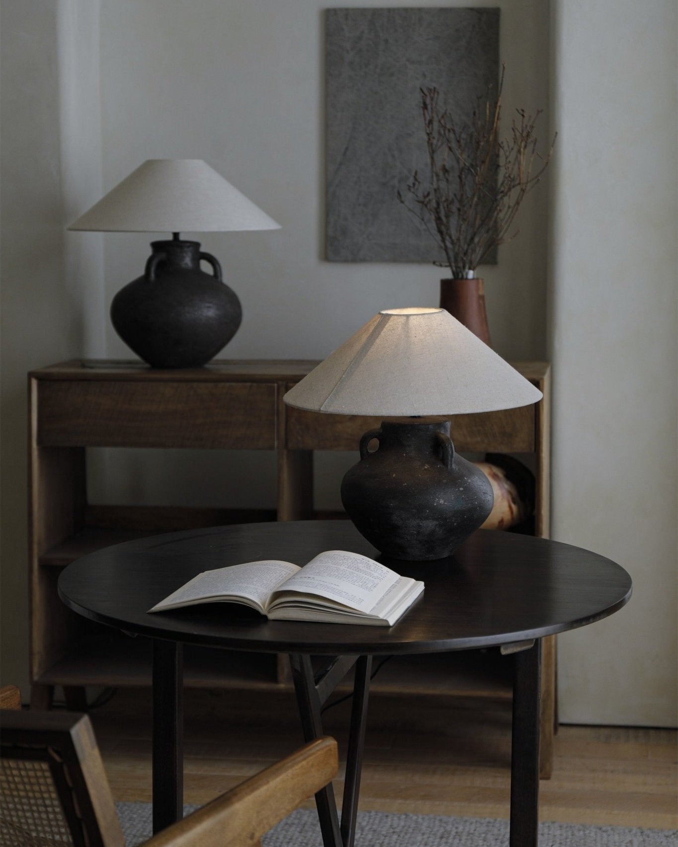 Ear lamp with dark clay base, off-white shade, and book on a round table.