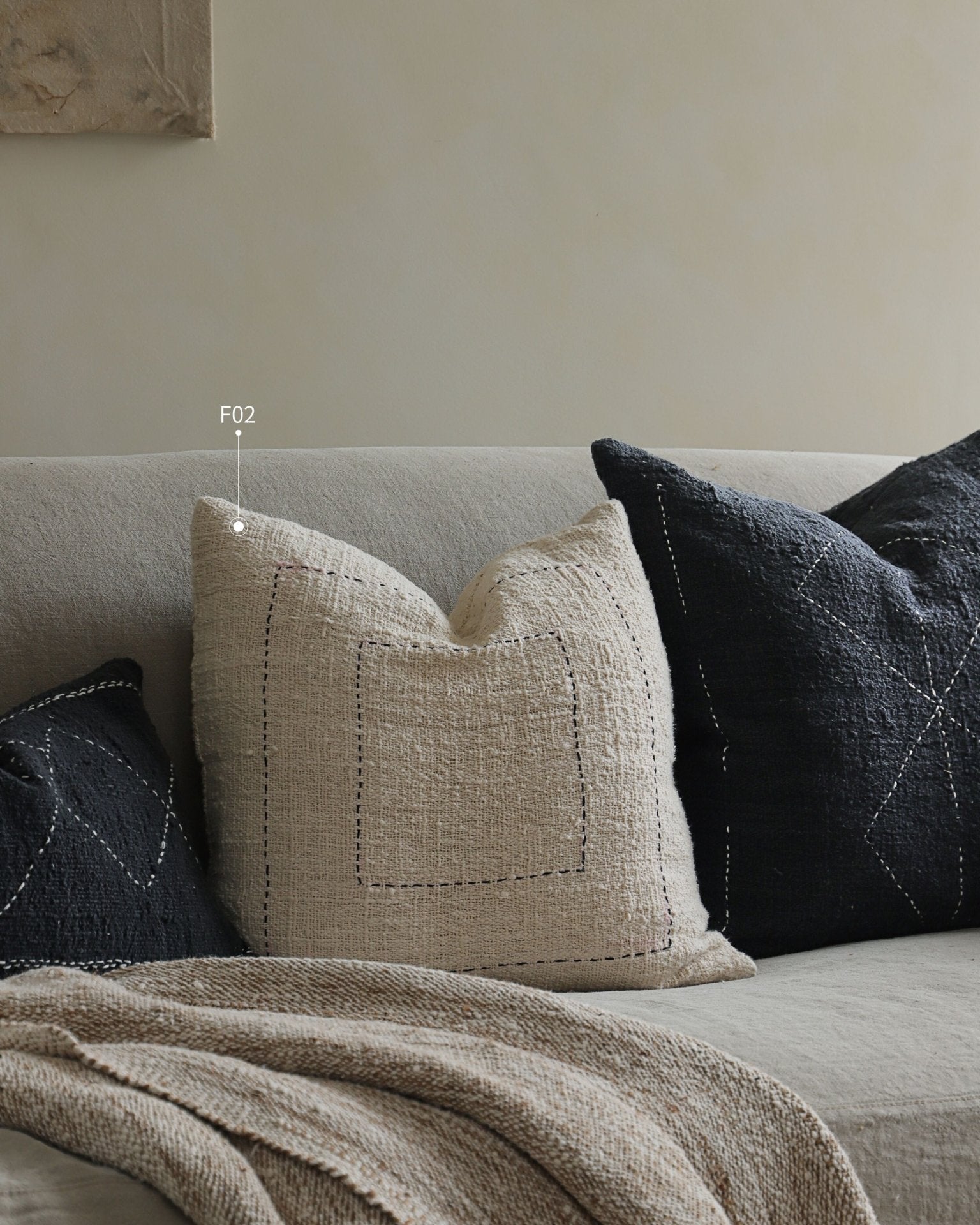 Cotton pillows in neutral colors on a couch, featuring beige and black pillows with stitched designs, "F02".