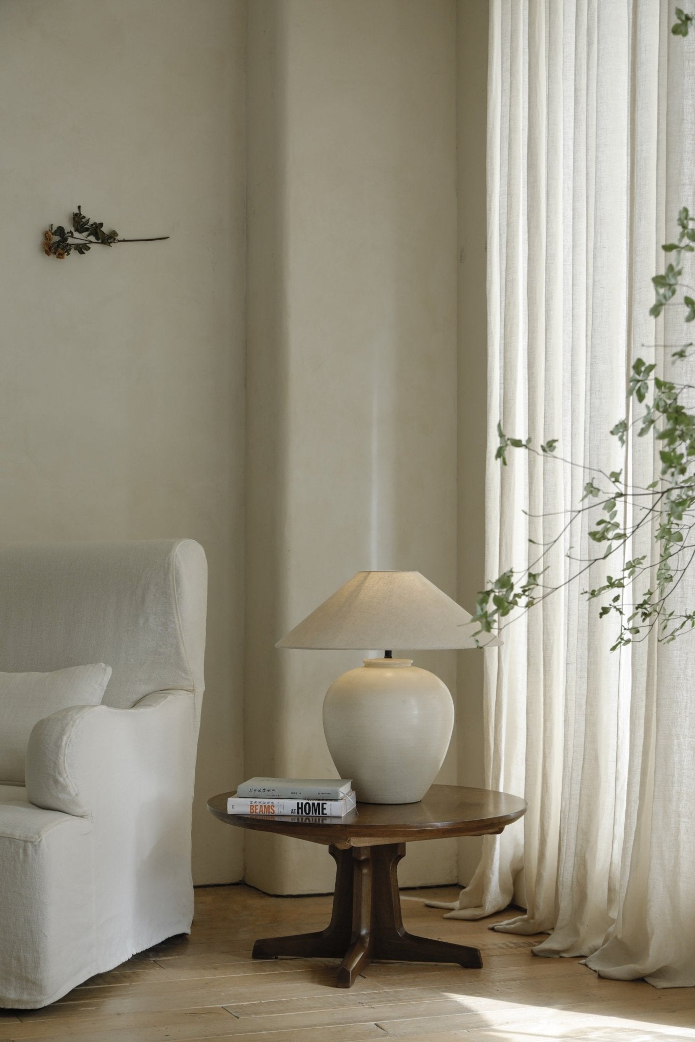 Egg Lamp on a wooden table beside a white sofa. Clay Egg Lamp with linen lampshade. BEAMS AT HOME books.