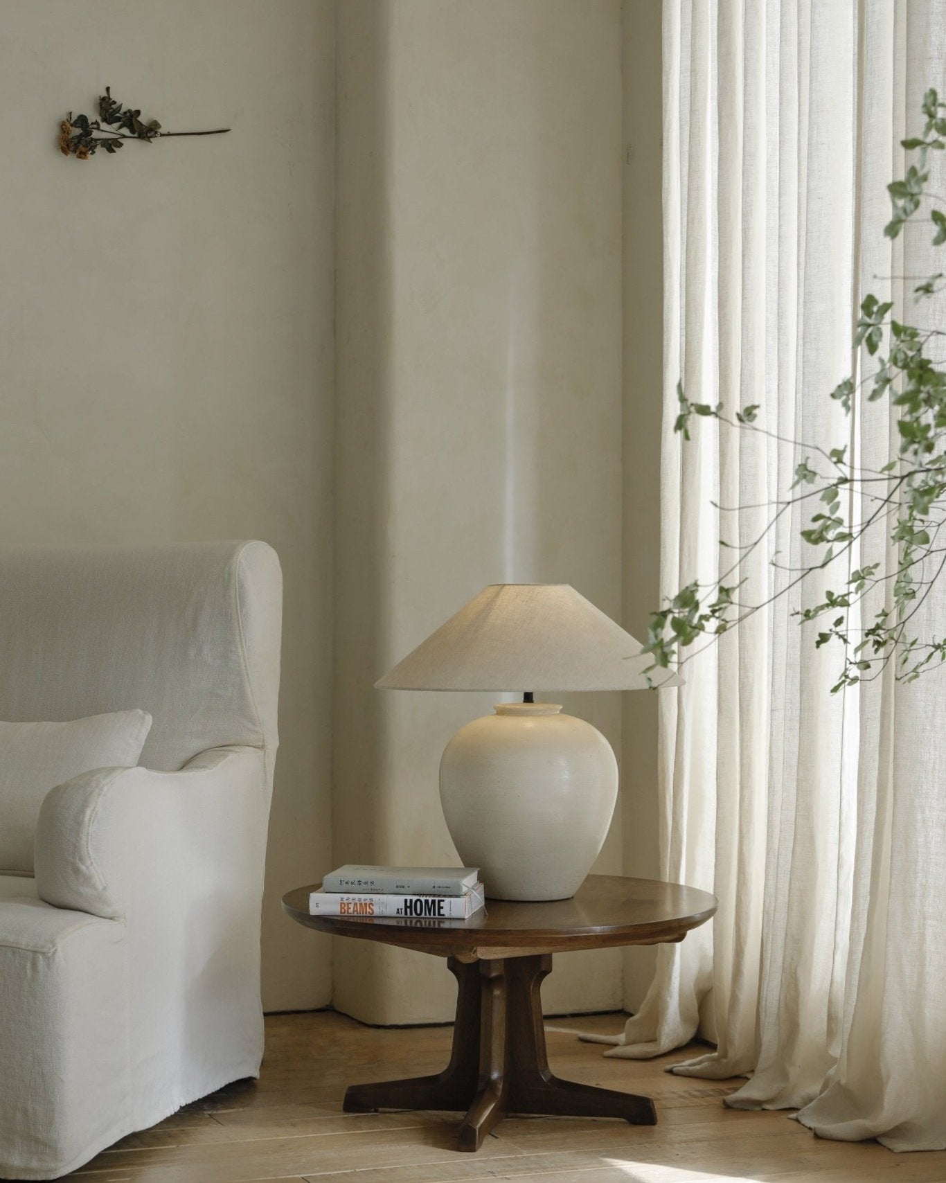 Egg Lamp on a wooden table beside a white sofa. Clay Egg Lamp with linen lampshade. BEAMS AT HOME books.