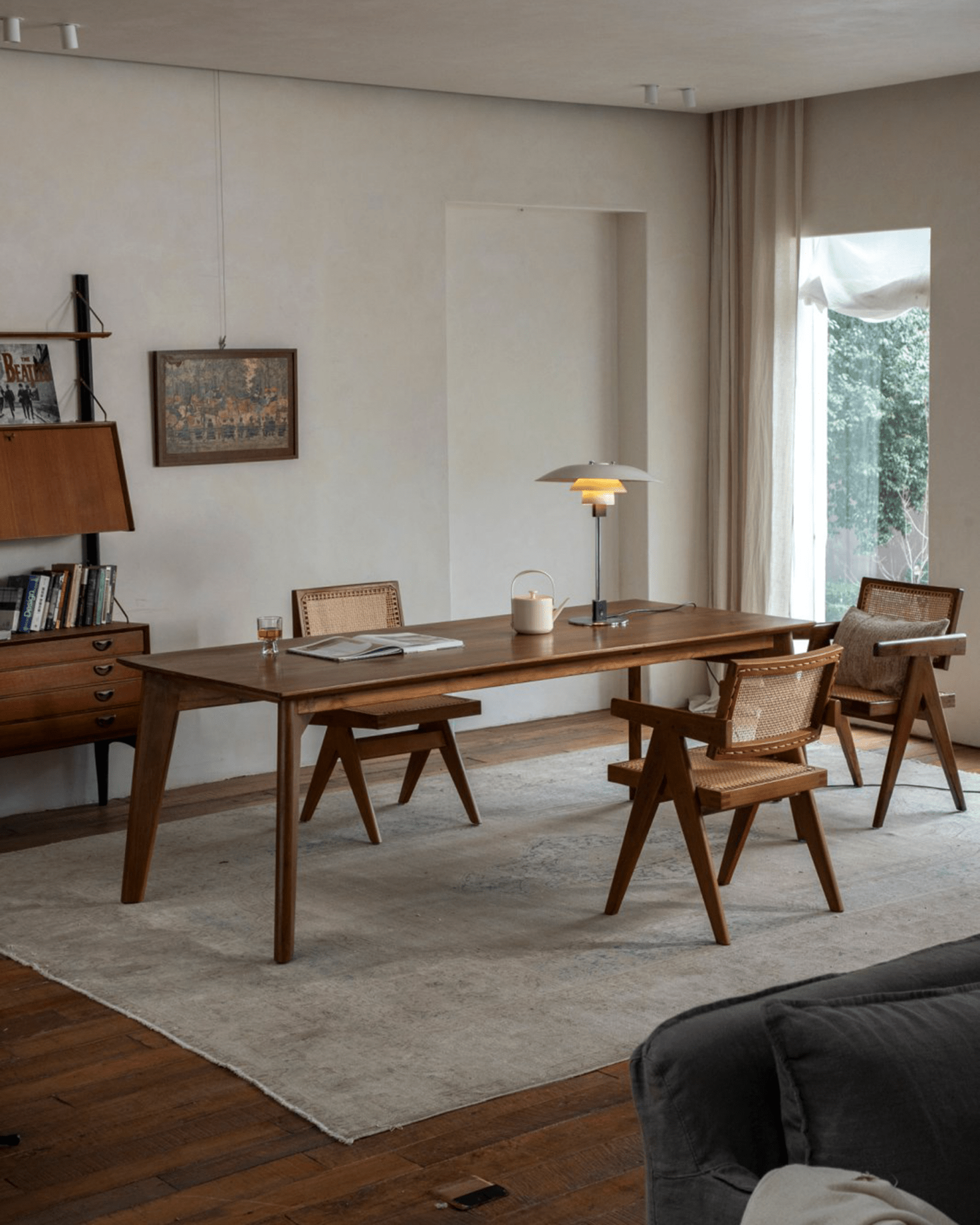 Mid-century modern dining room with a wooden table, Jeanneret-style cane chairs, and a vintage sideboard on a grey rug