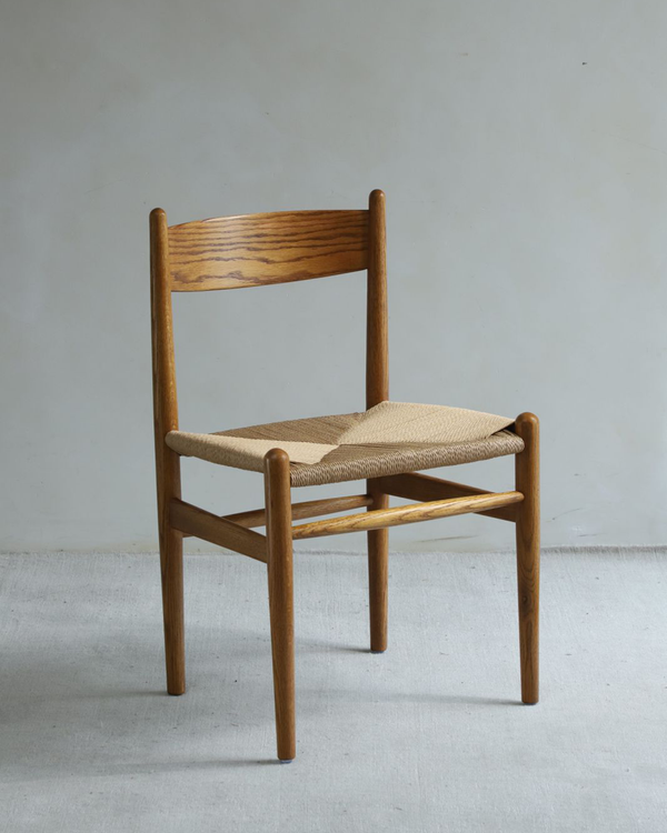 The CH No.36 Dining Chair by ZM Home, featuring a woven seat and simple backrest, is photographed against a plain light-colored wall and floor, highlighting its classic mid-century design.