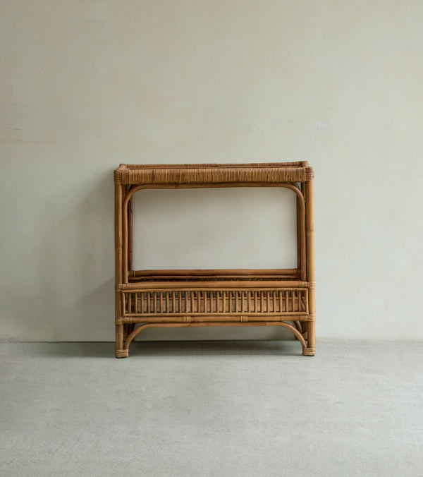 The Kaeo Rattan End Table by ZM Home is a rectangular console with double-layer storage and an open shelf, shown against a plain light-colored wall on a gray carpeted floor.