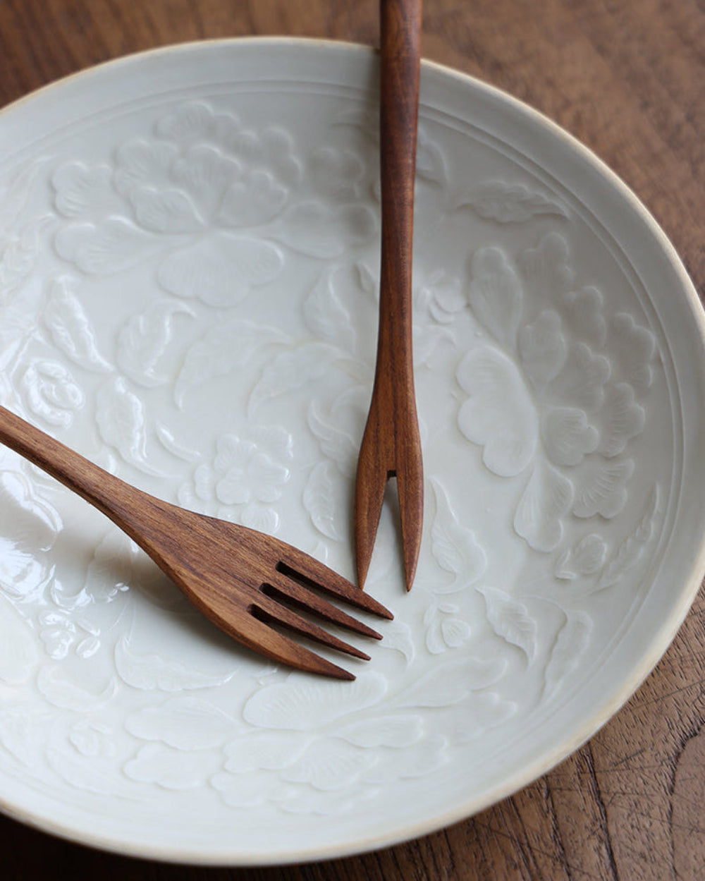 Wooden forks set on white plate with floral embossing, perfect for serving. Close up shot of the elegant cutlery.