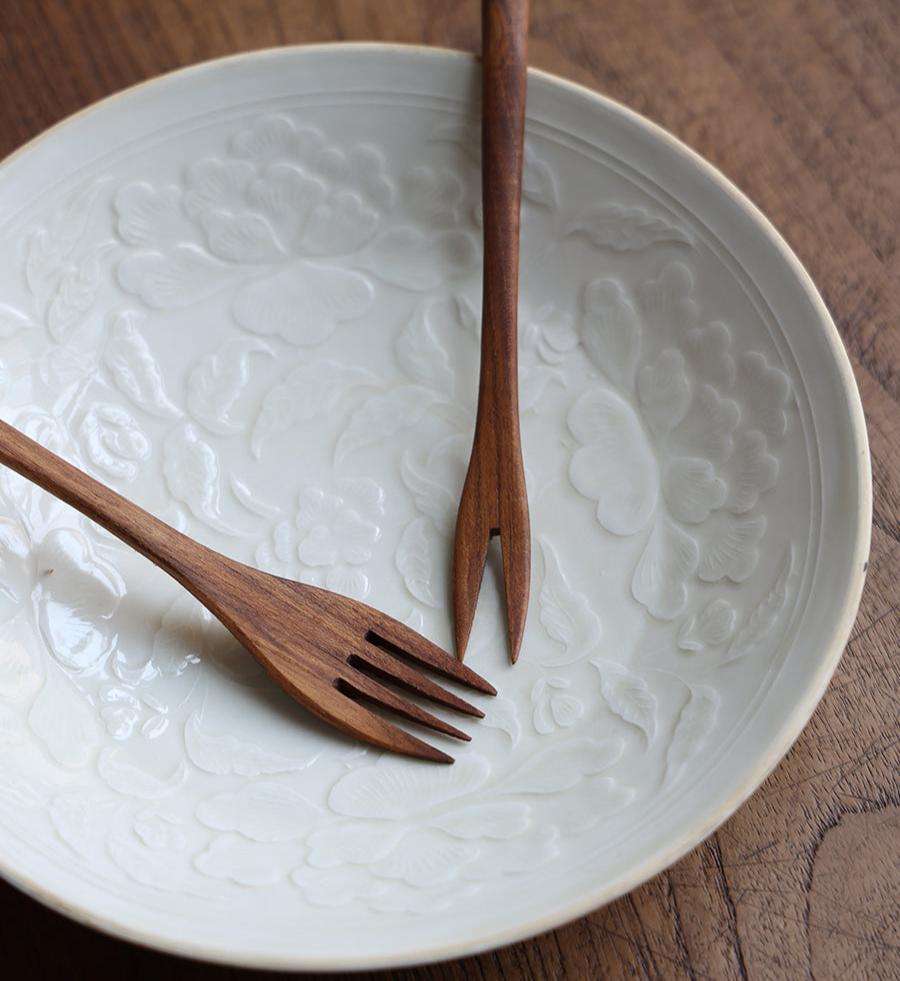 Wooden forks set on white plate with floral embossing, perfect for serving. Close up shot of the elegant cutlery.