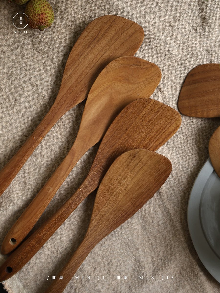 Wooden fried spatulas made by MIN JI on beige fabric, natural wood grain visible.