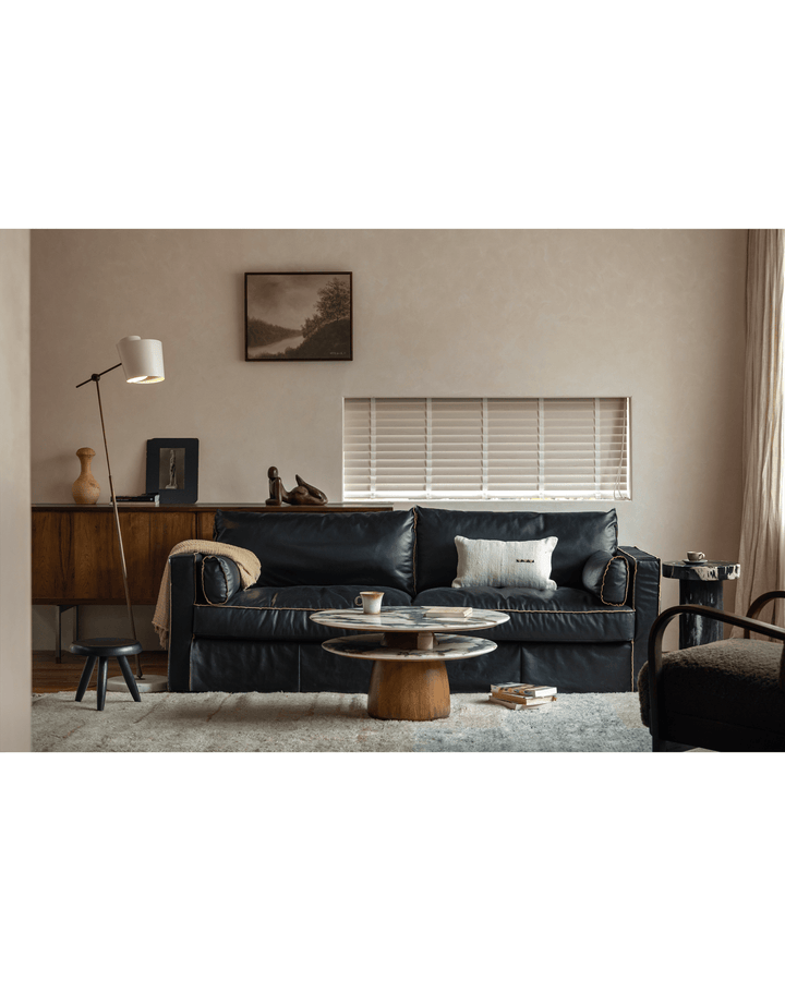 Stylish round marble side table with wooden base, cup, and book in modern living room.