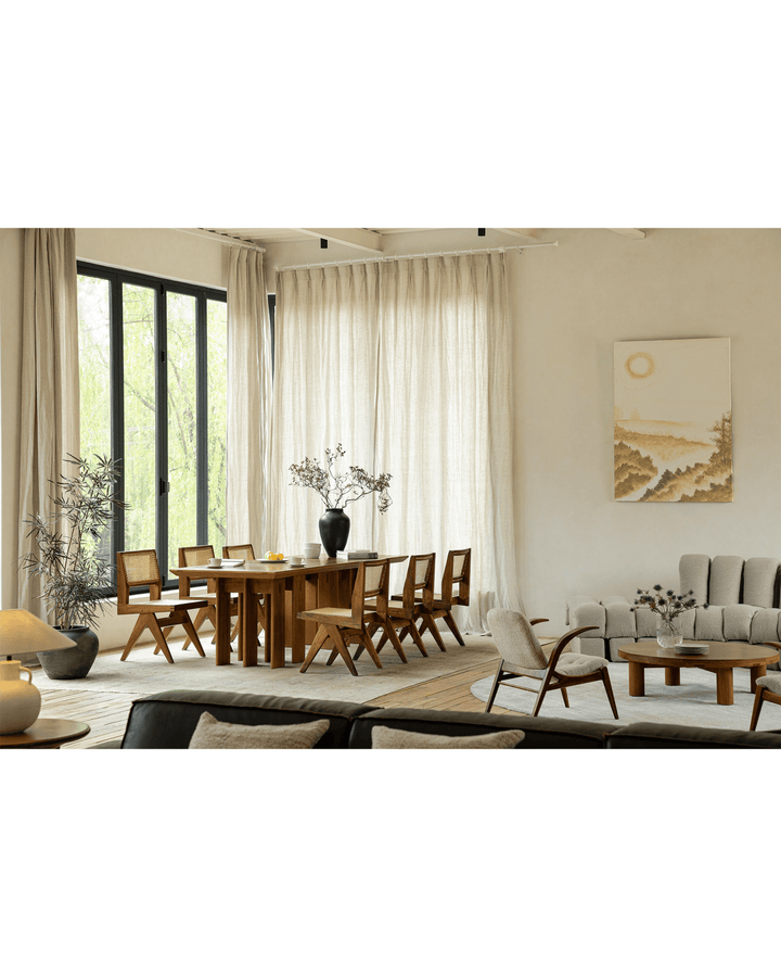 Spacious wooden dining table with chairs and flower vase in bright natural light.