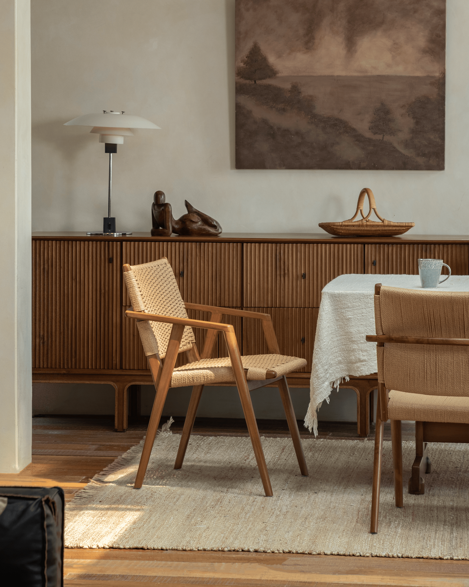 Louisa Chair in dining room setting. Teak frame and woven seat, Mid-Century Modern design, natural fiber rug.