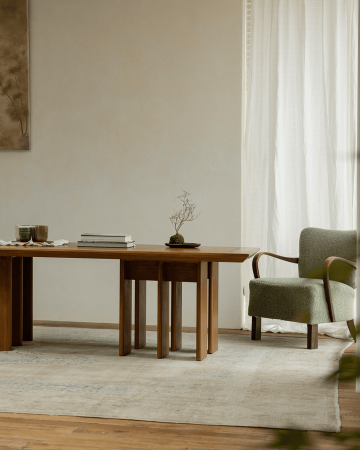 Modern wooden dining table with stacked legs, green chair, and decor in soft natural light.