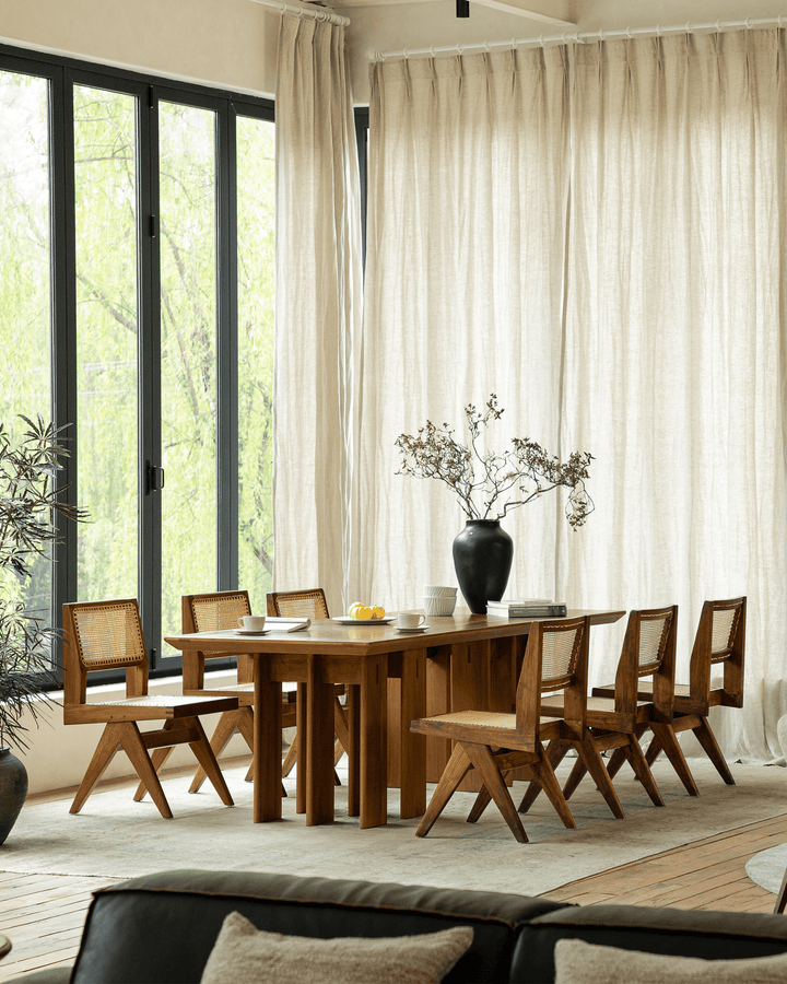 Stylish wooden dining table with six chairs and a vase in bright natural light