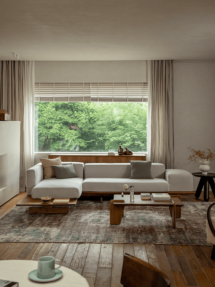 Bright minimalist living room with linen modular sofa and teak base overlooking green landscape.