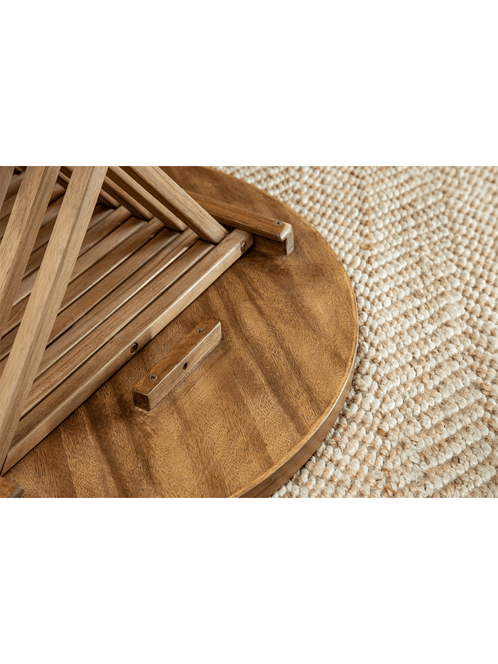Round folding coffee table with slatted base on a woven rug.