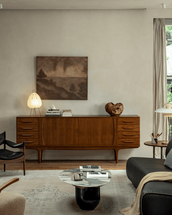 Vintage teak sideboard in a modern living room setup with artwork and lighting.