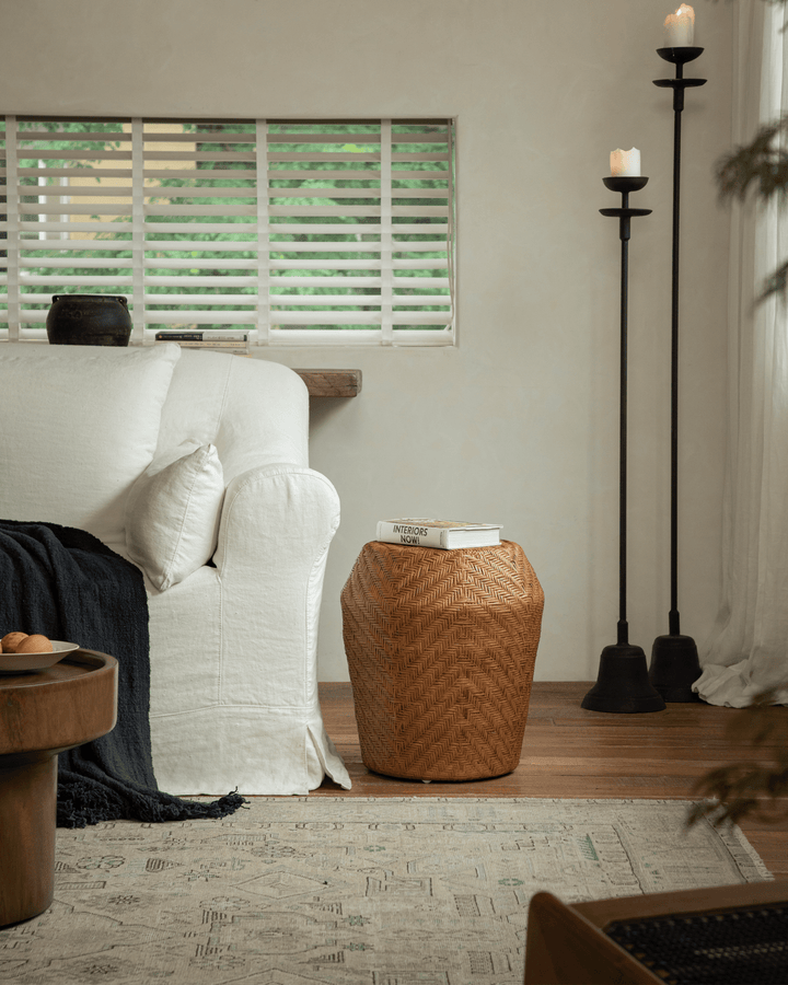 Drum Rattan Side Table beside a cozy sofa with a book on top in a warm living space