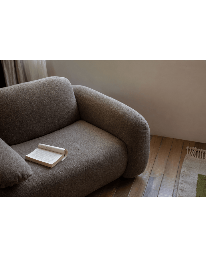 Cozy brown Gestein Bouclé Armchair with an open book on wooden floor.