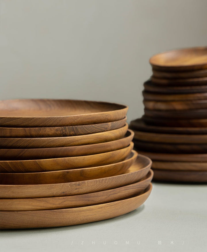 Stack of handcrafted oval teak wood plates with a smooth finish.