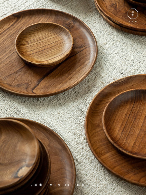 Handcrafted teak wood dinner plates and bowls on a textured surface.
