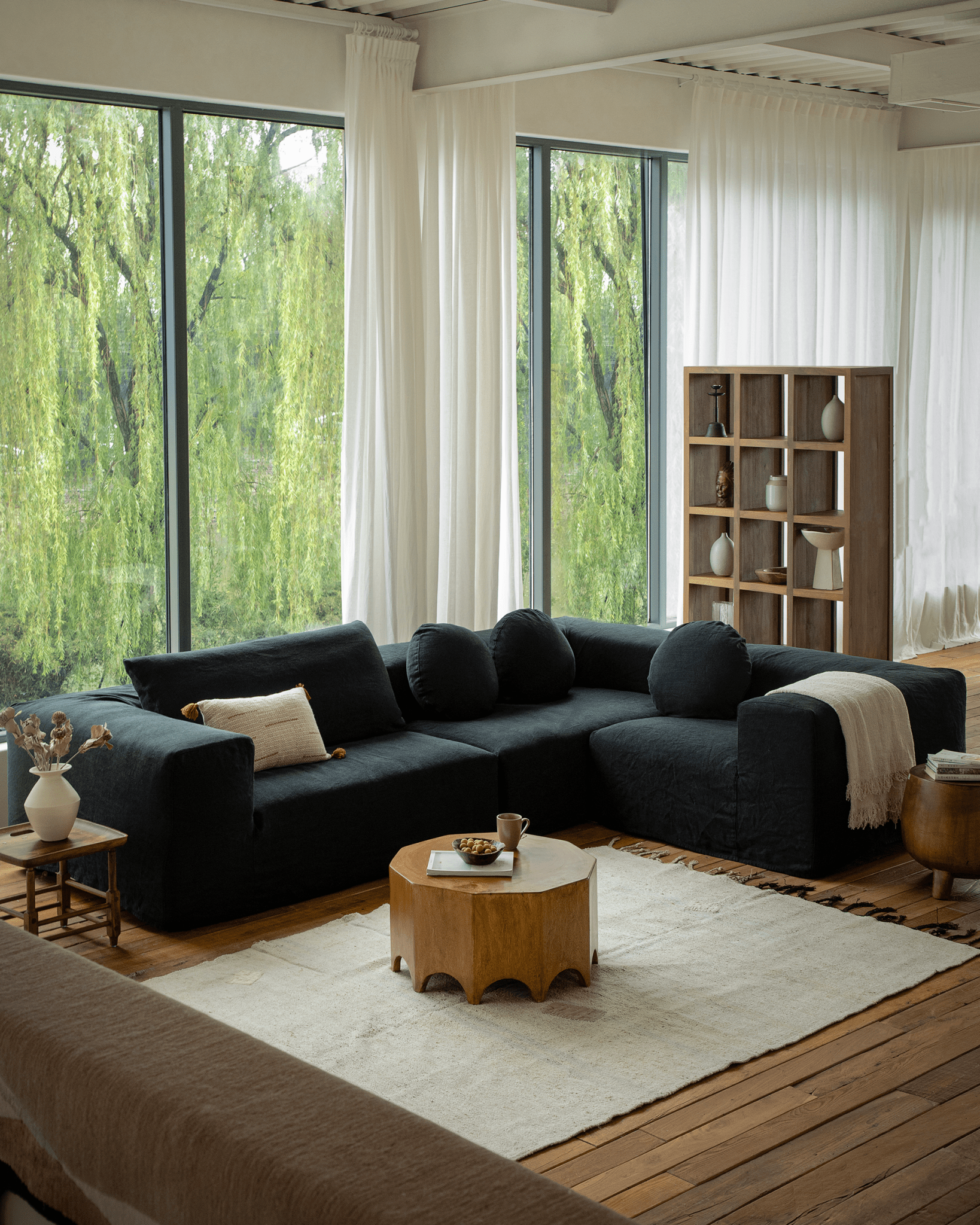 Living room with Decagon side table, dark sofa, rug, and large windows, showcasing modern interior design