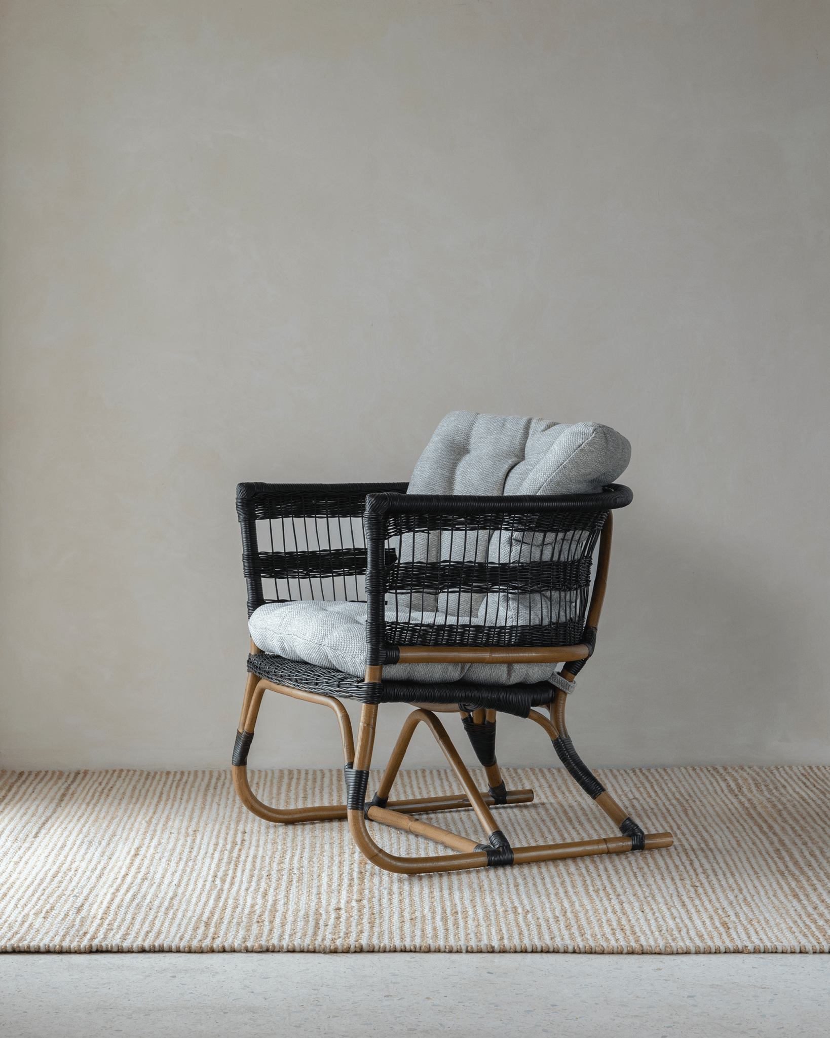Helian Rattan Chair with black frame, gray cushion, and a cozy interior setting