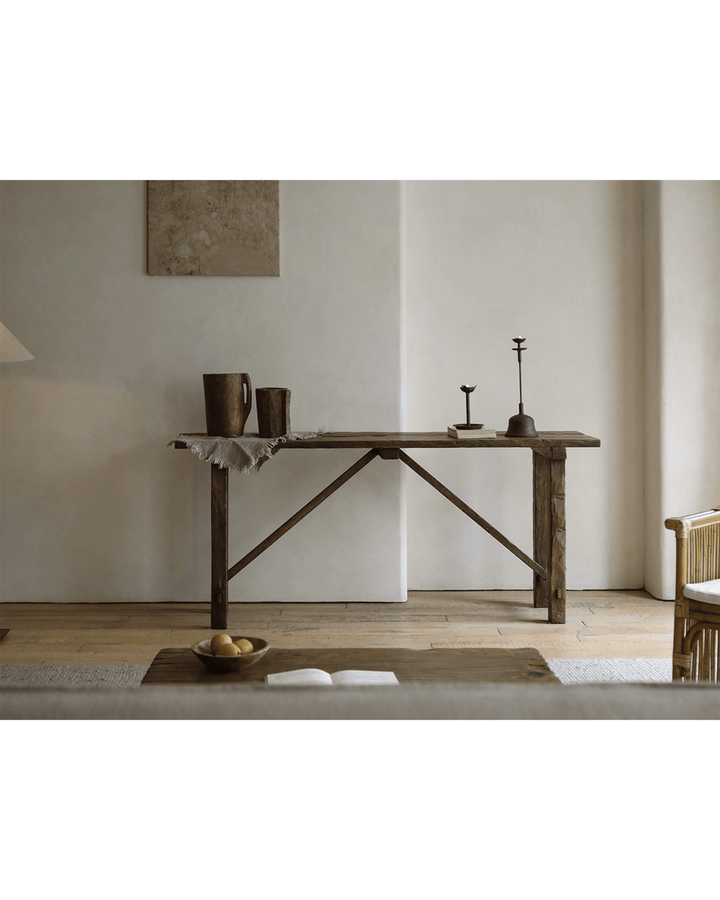Rustic K-Shaped console table with decorative items and candle holder in a minimalist setting.