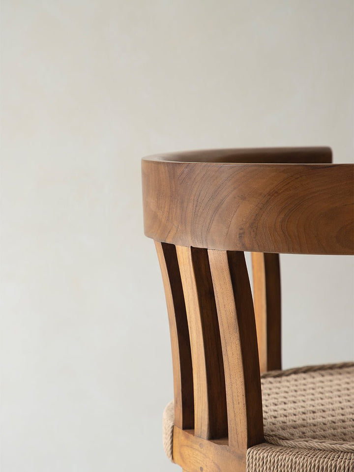 Curved back of ergonomic teak dining chair with woven seat detail.