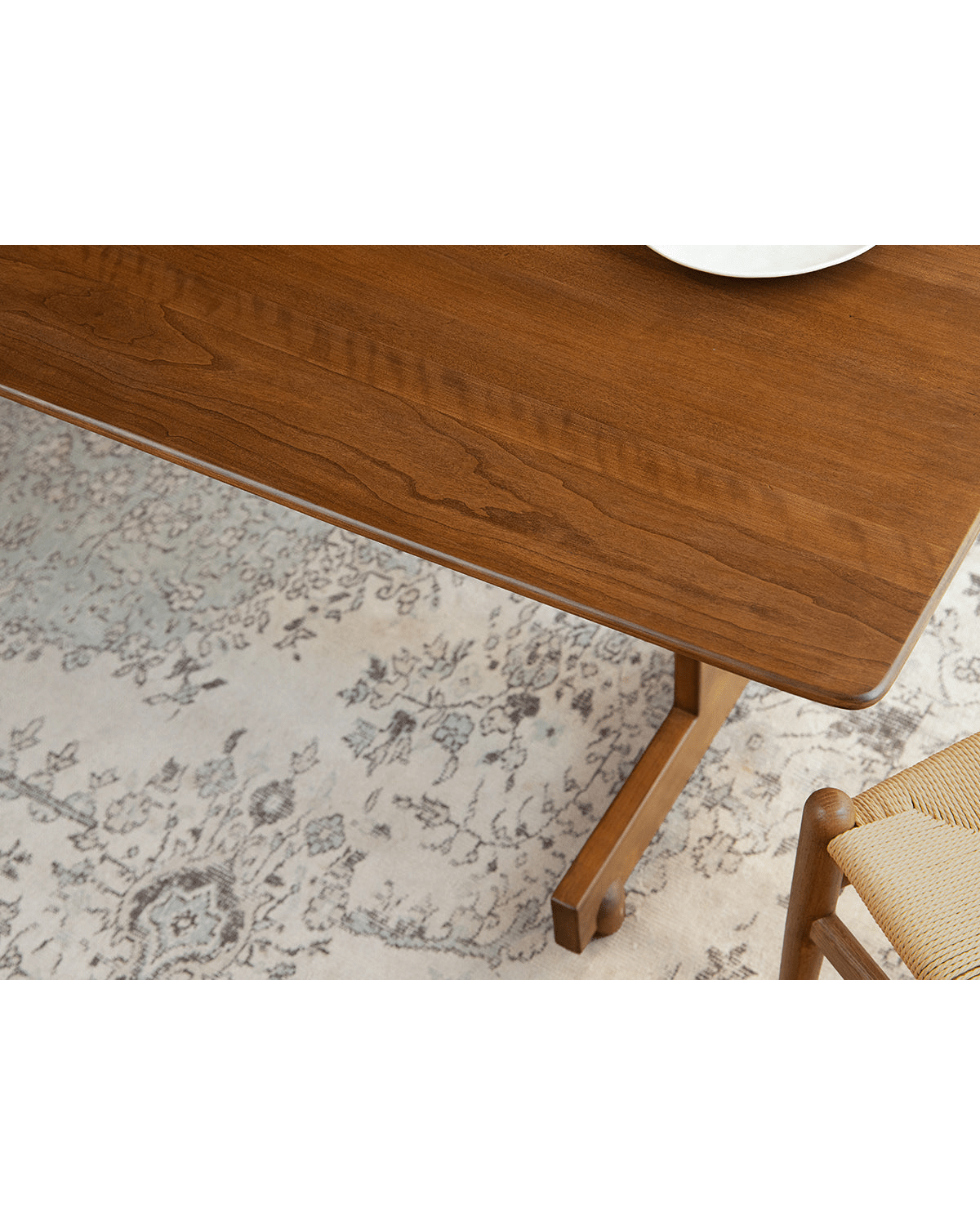 Hoof Dining Table with warm brown solid wood tabletop, I-shaped base, and woven chair in a dining setting.