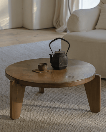 Round reclaimed wood coffee table with slanted legs, styled with teapot and cup