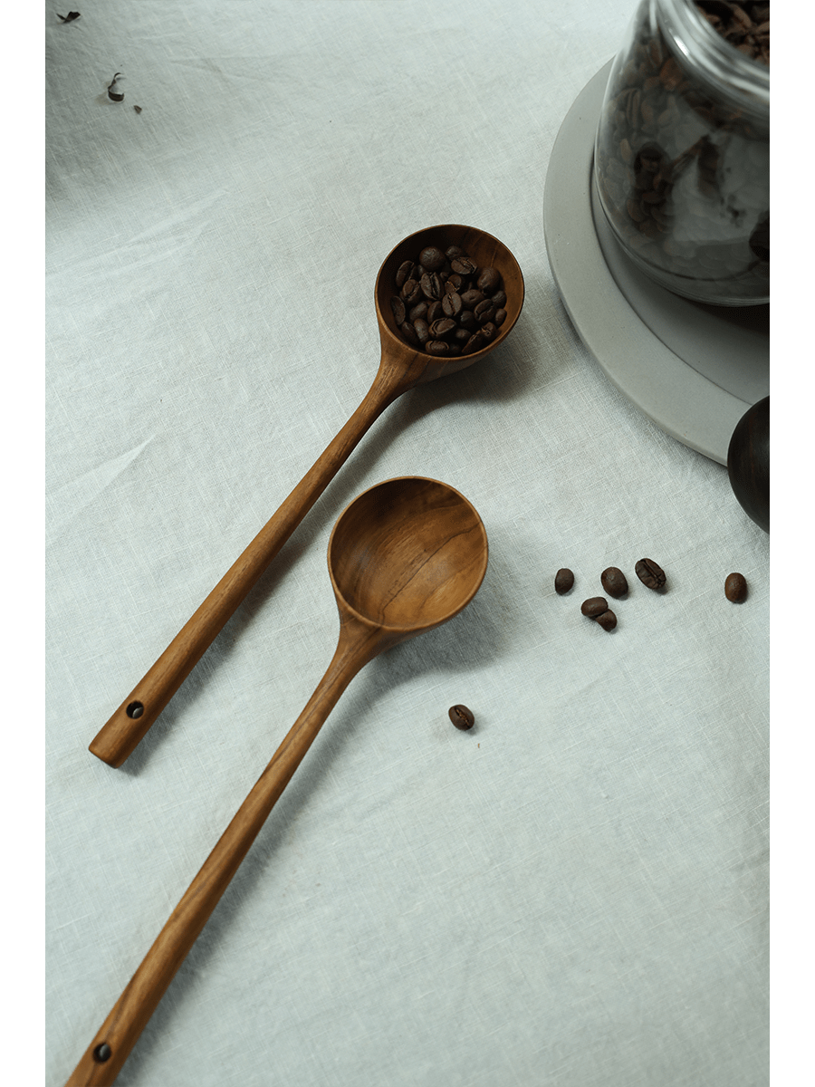 Teak coffee spoons on linen surface, one filled with coffee beans, ideal for serving coffee.