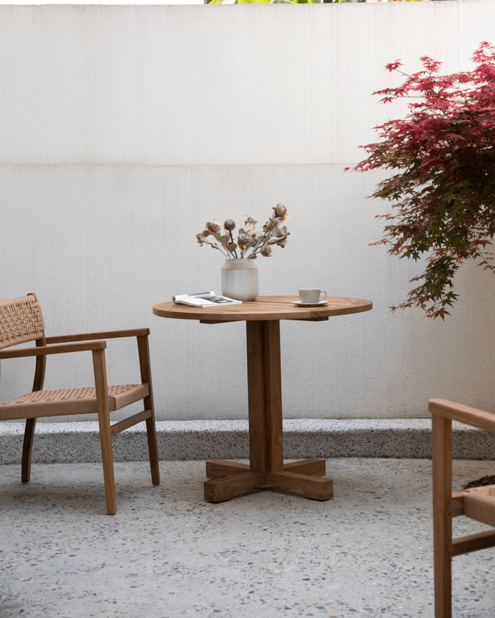 Ruby teak round table in a patio setting, with chairs and details perfect for dining or leisure