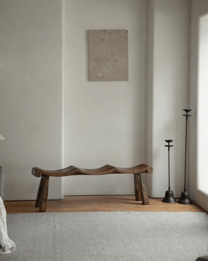 Tildes bench with wave-like wooden seat in minimalist room with decor items.