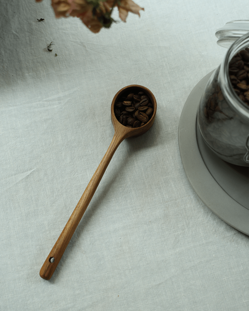 Teak coffee spoon filled with coffee beans, linen surface, for serving coffee.