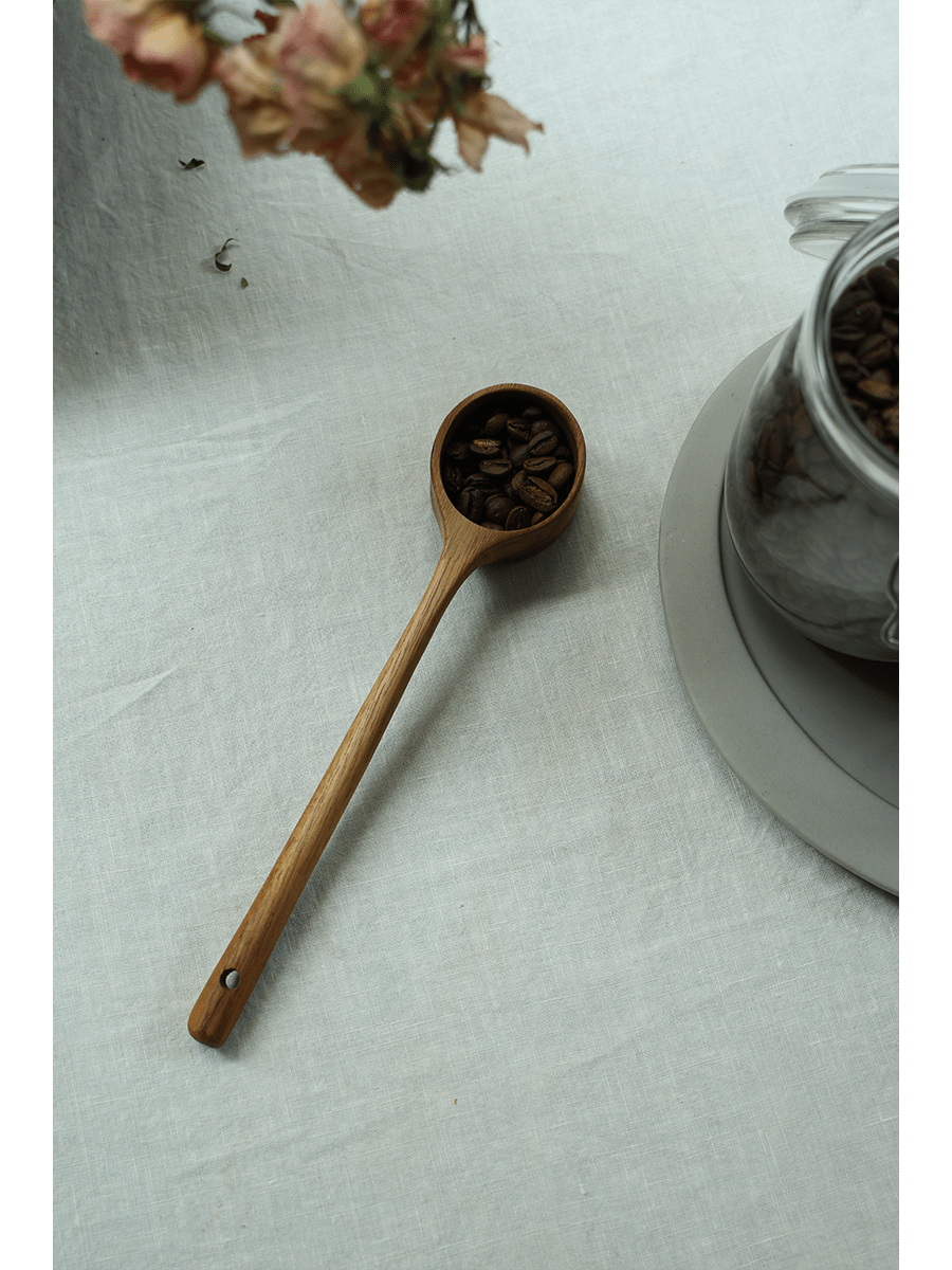 Teak coffee spoon filled with coffee beans, linen surface, for serving coffee.