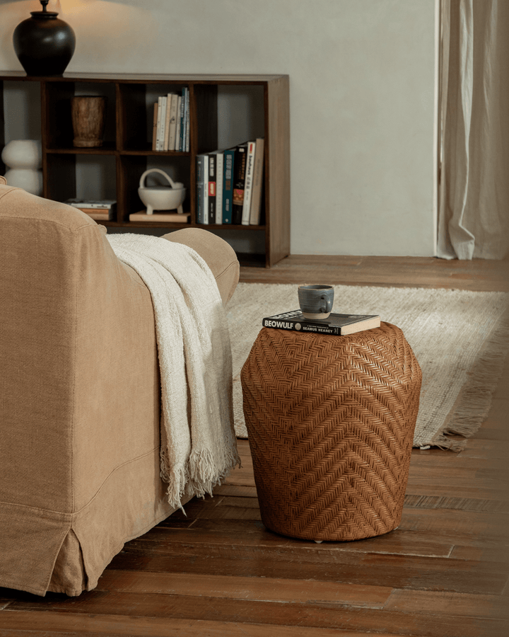 Drum Rattan Side Table with a cup and book next to a sofa in a warm living room