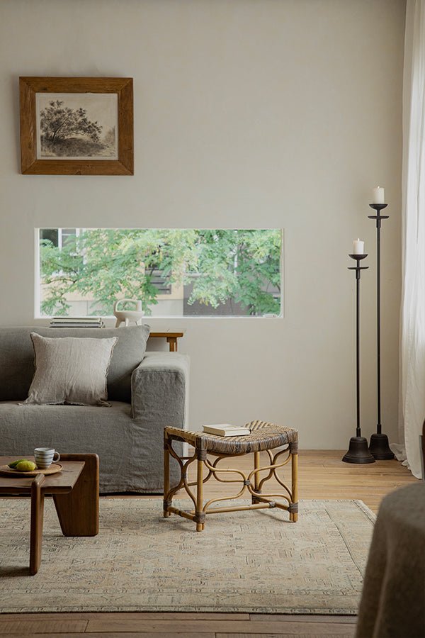 Melange Stool in Manau rattan next to a gray sofa and decorative rug in a sunlit room