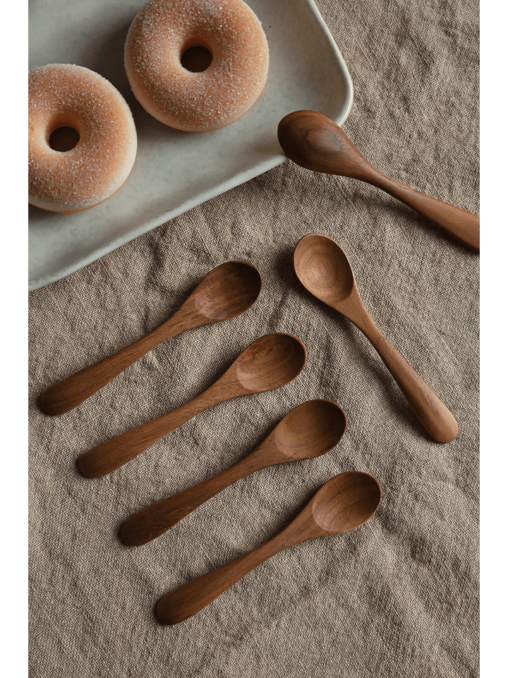 Set of six wooden spoons beside donuts on burlap fabric