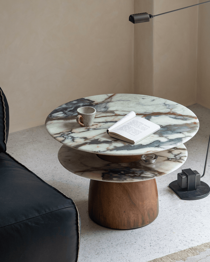 Round marble side table with wooden base, cup, and open book in a modern living space